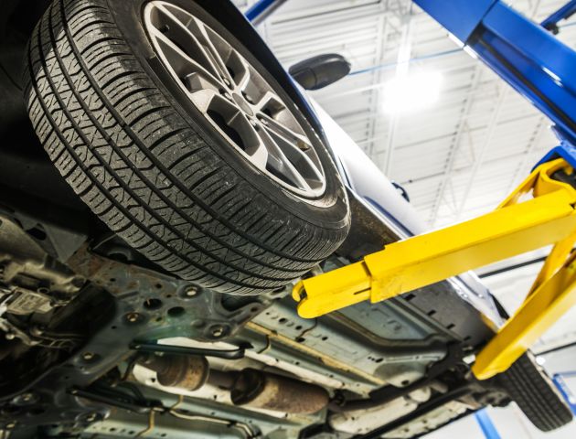Broken Modern Car on an Automotive Lift Inside Auto Service Center Undercarriage Close Up. Automotive and Transportation Industry Theme.