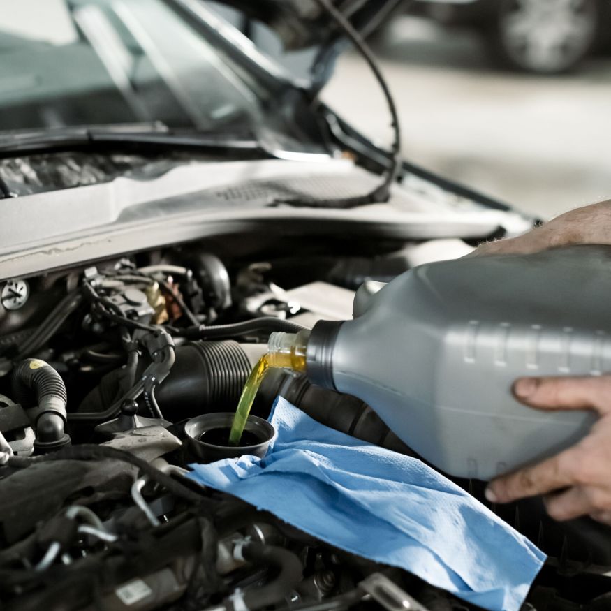 Service mechanic pouring new synthetic or organic oil lubricant into the car engine. Fresh oil poured during an oil change to a car